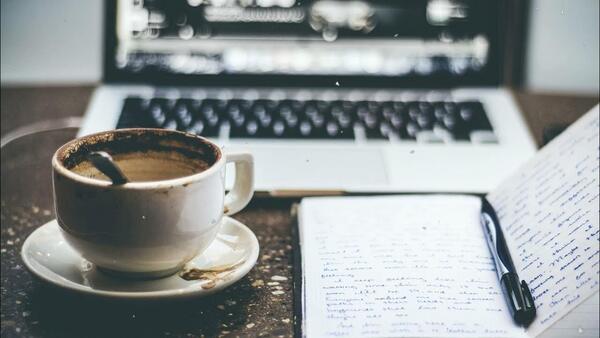 A cozy workspace with a notebook, pen, and warm drink on a wooden table